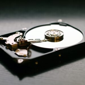 An open hard drive is displayed on a wooden surface, showcasing its internal components and metallic details.